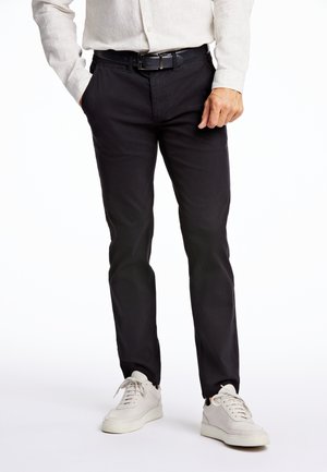 Schwarze Chinos aus Baumwolle, mit slim fit, Seitentaschen und einem Gürtel, kombiniert mit weißen Turnschuhen. Glatte Textur und klare Linien.