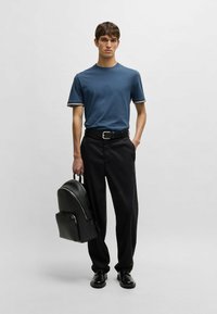 Blå bomullströja med vit kant, svart bälte, svarta byxor och en texturerad svart ryggsäck med en böjd form och dragkedja.