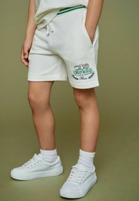 Witte katoenen shorts met zijzakken, een trekkoord in de taille en een groen geborduurd "Smiley World" logo met tennis-gerelateerde grafische afbeeldingen.