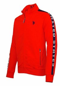 Röd zip-up jacka med marinblå ränder på ärmarna, texten "Förenta staterna", dragkedjefickor och en liten hästlogotyp på bröstet.