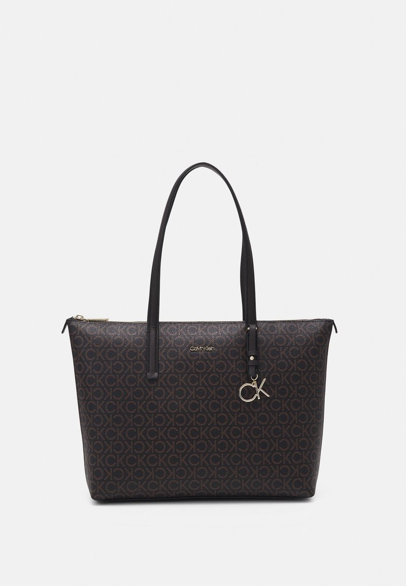 Sac cabas Calvin Klein marron foncé avec motif à logos CK répétés, breloque CK dorée et deux longues poignées noires.