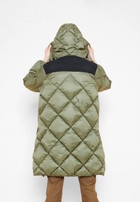 Cappotto imbottito trapuntato verde con pannello nero sulla spalla e cappuccio, presenta un motivo a diamante e una texture lucida, che arriva fino a metà coscia.