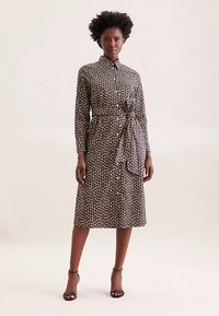 Schwarz-beiges Kleid mit Leopardenmuster, Kragen, langen Ärmeln, Taillengürtel und knielangem A-Linien-Schnitt.