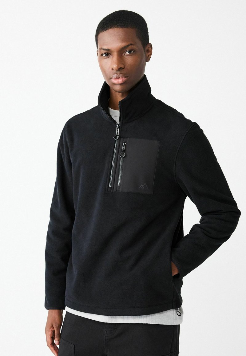 Pullover in pile nero con collo alto, mezza zip frontale e tasca sul petto con cerniera. Presenta una finitura testurizzata e spacchi laterali.