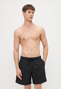 Svarte svømmebukser med teksturert mønster, elastisk midjebånd og snor. Behagelig passform med sidelommer og avslappet design.