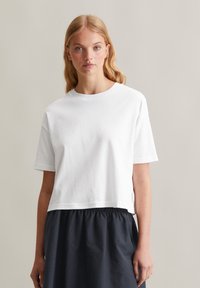 T-shirt en coton blanc avec une coupe décontractée, col rond et manches courtes, associé à une jupe fluide foncée. Design simple et minimaliste.