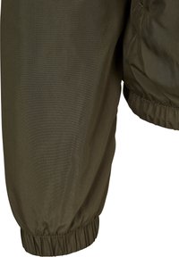 Gros plan sur une jambe en tissu vert olive avec poignet élastique, partie d'un vêtement, montrant les coutures et les détails du tissu froncé.