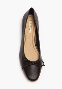 Ballerine en cuir noir avec un bout pointu, dotée d'un mince nœud décoratif à l'avant et d'une semelle intérieure rembourrée beige avec des détails de couture.