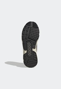 Skosula med en svart gummibas, mönstrad med cirkulära och rektangulära mönster, med ljusa detaljer och en perforerad sektion.