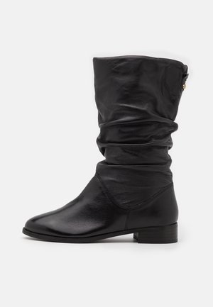 Black mid-calf leather boot with slouched shaft, low stacked heel, rounded toe, and subtle zipper detail near the top edge.