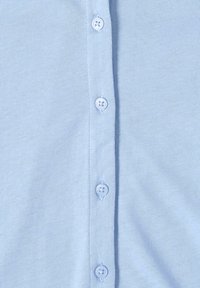 Hellblaue Button-Down-Bluse aus weichem, strukturiertem Stoff. Verfügt über fünf passende Knöpfe auf der Vorderseite zum Schließen.