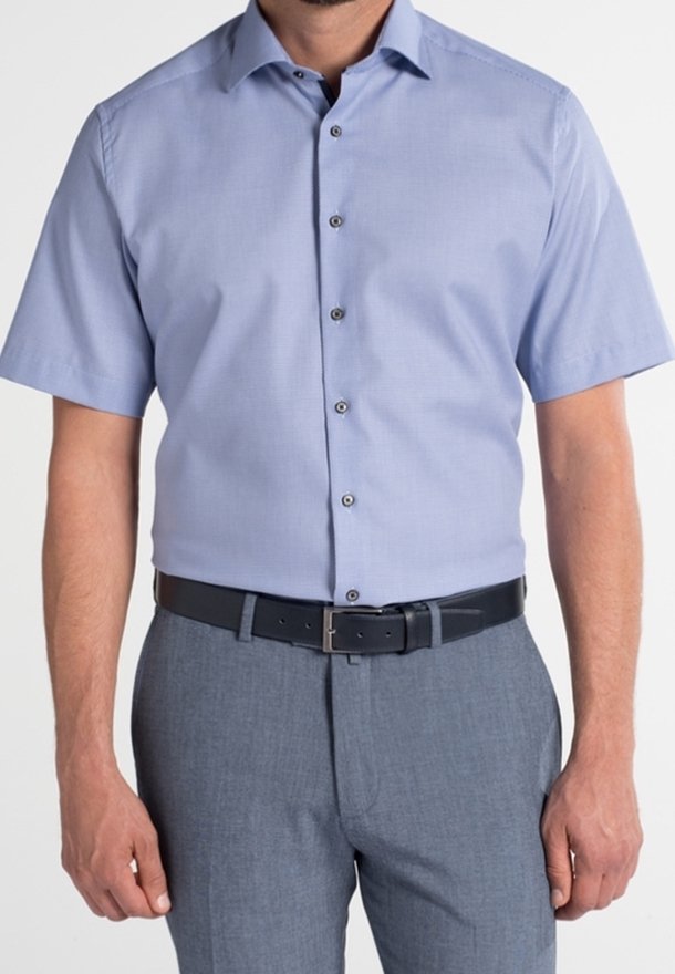 Chemise bleu clair à manches courtes avec un col boutonné, présentant une texture subtile et des boutons foncés, accompagnée d'un pantalon de costume gris et d'une ceinture noire.