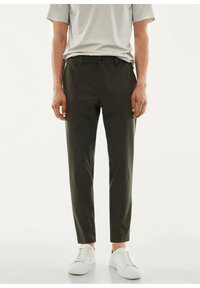 Slim-fit trousers in dark olive green fabric, characterized by a smooth texture, belt loops, and front pockets, paired with white sneakers.