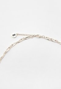 Collana in argento con maglie piatte allungate, piccoli accenti sferici e un'etichetta circolare con il logo. Include una chiusura a moschettone.