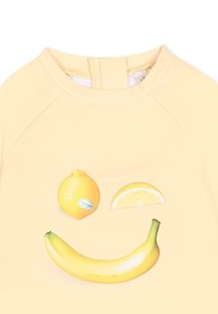 Jasnożółta koszula z uśmiechniętą buźką wykonaną z cytryny, plasterka cytryny i banana na przedzie.