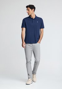 Mörkblå pikétröja med knäppning i tre knappar, kombinerad med ljusgråjeans och beige sneakers. Slätt tyg och moderna passformdetaljer.