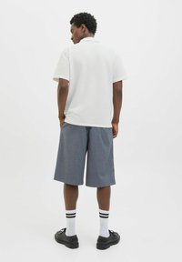 Hvid tekstureret polo t-shirt, grå shorts til knæene, sorte sko og hvide sokker med sorte striber. Bagfra, minimalistisk design.