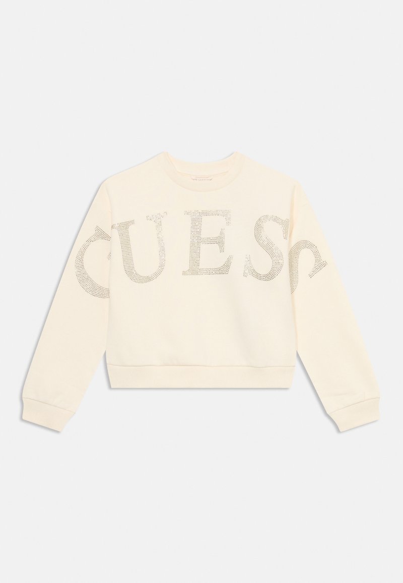 Sweat-shirt à manches longues couleur crème avec de grandes lettres en strass formant le mot "GUESS" sur le devant et les manches.