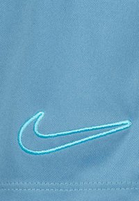 Tejido atlético de color azul claro con un logo de Nike bordado en turquesa. Textura suave con un detalle de tejido sutil.