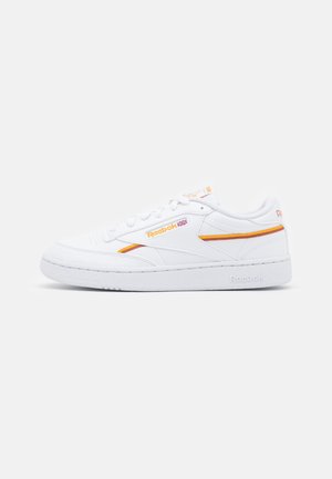 Biały niski sneaker Reebok z pomarańczowo-żółtymi detalami w postaci pasków oraz z logo marki na boku i pięcie, przedstawiony na jednolitym tle.