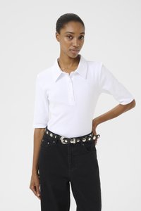 Hvit kortermet polo skjorte med krage og seks knapper, kombinert med høyt liv svarte jeans og et naglet svart belte.