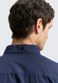 Camicia a quadri blu navy con colletto strutturato, caratterizzata da un piccolo bottone nero sul retro del collo e tessuto testurizzato.