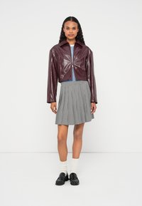 Veste en vinyle bordeaux raccourcie avec fermeture à pression, associée à une jupe plissée à carreaux noir et blanc, des chaussettes blanches et des chaussures noires.