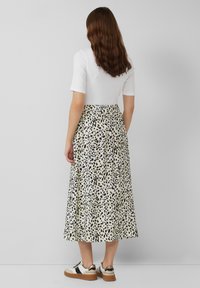 Midi rok in crèmekleur met zwart gespikkelde luipaardprint, gecombineerd met een aansluitend wit topje en instapsneakers. Glad materiaal met een elastische tailleband.