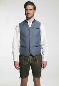 Traditionelles bayerisches Outfit mit einer blauen gemusterten Weste mit schwarzen Akzenten und einem weißen Hemd, kombiniert mit dunklen braunen Lederhosen mit dekorativen Nähten.