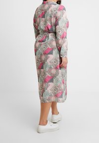 Une robe à manches longues, avec un motif mélangeant des couleurs rose, gris et vert, dotée d'une taille ceinturée et d'une longueur mi-mollet.