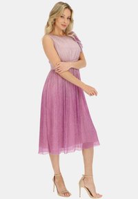 Różowo-fioletowa sukienka z gradientem, z dopasowanym gorsetem, rozkloszowanym spódnicą i falbaną na jedno ramię. Tkanina ma błyszczącą fakturę.