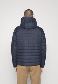 Marinblå pufferjacka med horisontell quiltning, hög krage och figurnära design. Har en huva och ribbade muddar. Slätt, lättviktsmaterial.
