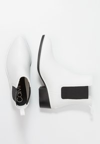 Botas blancas hasta el tobillo con punta afilada, material sintético suave, paneles laterales elásticos negros y un tacón bajo tipo bloque. Diseño minimalista.