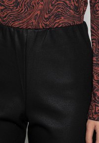 Pantalons noirs texturés avec une taille élastique, associés à un haut à manches longues arborant un motif marbré rouge et noir.