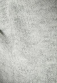 Vaaleanharmaa neulottu kangas, jossa on pehmeä ja teksturoitu pinta. Materiaali vaikuttaa lämpimältä ja kutsuvalta, ja siinä on hienovaraisia värivaihteluita.