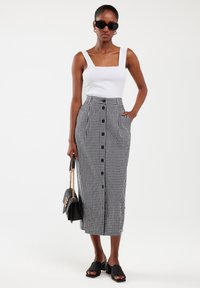 Weißes Top mit quadratischem Ausschnitt, kombiniert mit einem langen Rock aus schwarz-weißen Karos, der über eine vordere Knopfleiste verfügt, accessorized mit einer schwarzen Handtasche.