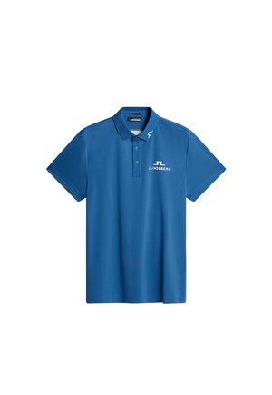 Blå polo skjorte lavet af glat stof, med en tre-knaps lukning og hvidt logo på venstre bryst. Korte ærmer med klassisk krave.