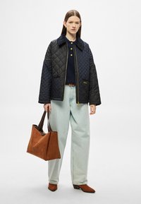 Μπουφάν καπιτονέ μαύρο με μπλε γιακά, συνδυασμένο με μπλε πουκάμισο, ανοιχτό μπλε παντελόνι και καφέ τσάντα ώμου από σουέτ. Καφέ μπότες με τακούνι.