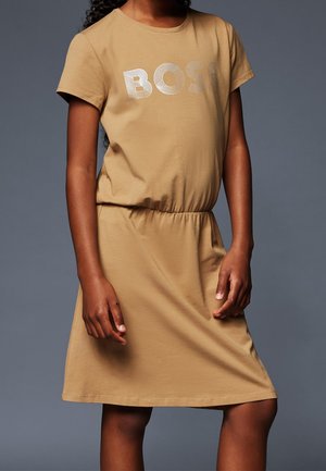 Beżowa sukienka do kolan wykonana z miękkiego materiału, z krótkimi rękawami i elastyczną talią. Z przodu znajduje się metaliczne logo "BOSS".