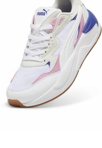 Białe sneakersy Puma z różowymi i niebieskimi akcentami, wykonane z siatkowego i syntetycznego materiału, z okrągłym czubkiem, wyściełanym kołnierzem i teksturowaną gumową podeszwą.