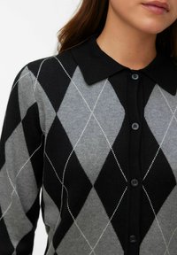 Svart och grå argyle-kofta med krage, knappar fram och strukturerat stickat mönster med vita diamantkonturer.