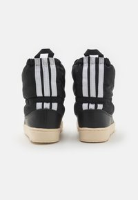 Černé tenisky s vysokým svrškem, s texturovanou koženou základnou, elastickým látkovým svrškem, bílými proužky a béžovými gumovými podrážkami.
