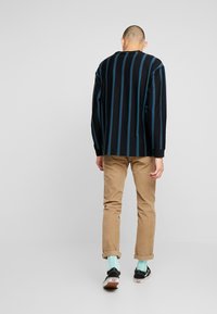 Svart långärmad skjorta med blå vertikala ränder, beiga byxor, svarta sneakers och ljusblå strumpor. Enkel, avslappnad passform.