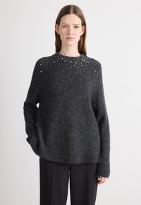 Pull en maille gris foncé avec une surface texturée et un col rond, présentant des éclats de lumière éparpillés et des poignets et un ourlet côtelés.