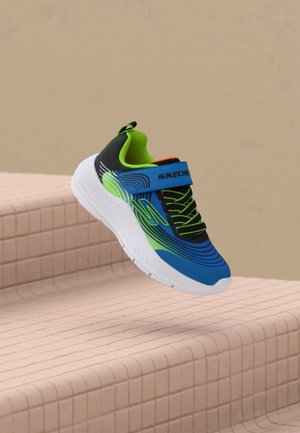 Dziecięcy niebiesko-zielono-czarny sneaker Skechers z białą podeszwą i paskiem na rzep unoszący się nad różowymi kafelkowanymi schodami.