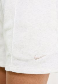 Shorts en coton de couleur claire avec une texture douce, présentant un logo Nike beige subtil sur l'ourlet. Design simple, coupe mi-longue.