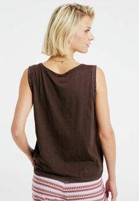 Top marrón sin mangas con un corte relajado, escote redondo y una textura sutil. Combinado con pantalones de colores multicolores con detalles intrincados.