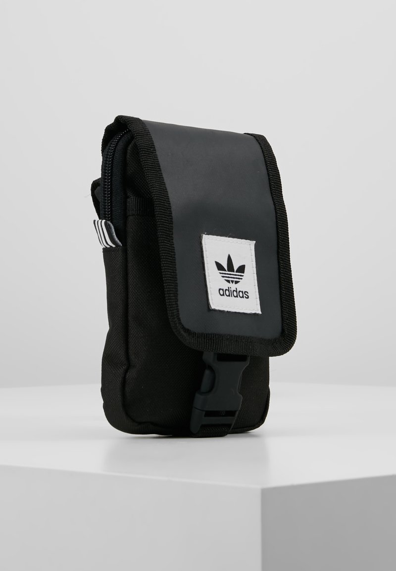 Pochette in tessuto nero con patta pieghevole, dotata di un'etichetta con logo Adidas bianco e una chiusura a clip. Rifinita con dettagli a righe bianche e nere.