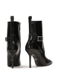 Botines negros de tacón alto hechos de cuero brillante. Presentan un cierre con cremallera, una correa con una hebilla cuadrada y punteras afiladas.