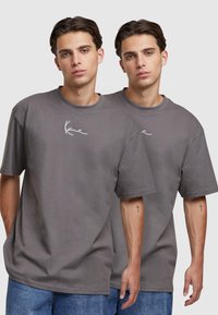 Siva oversized majica od pamuka s okruglim izrezom i kratkim rukavima. Ima bijeli potpisani logo na prsima.